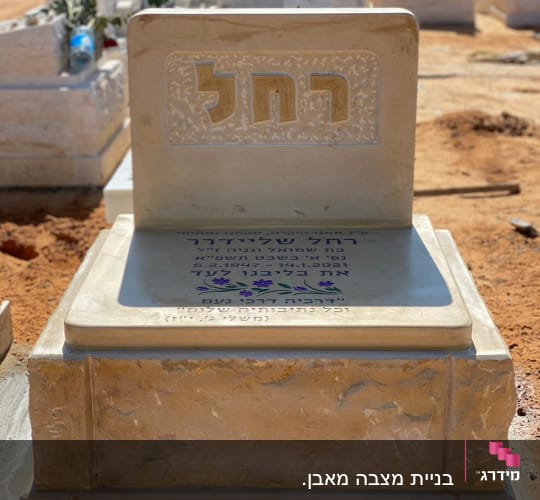 מצבה עם כיתוב בעברית ופרחים מסביב